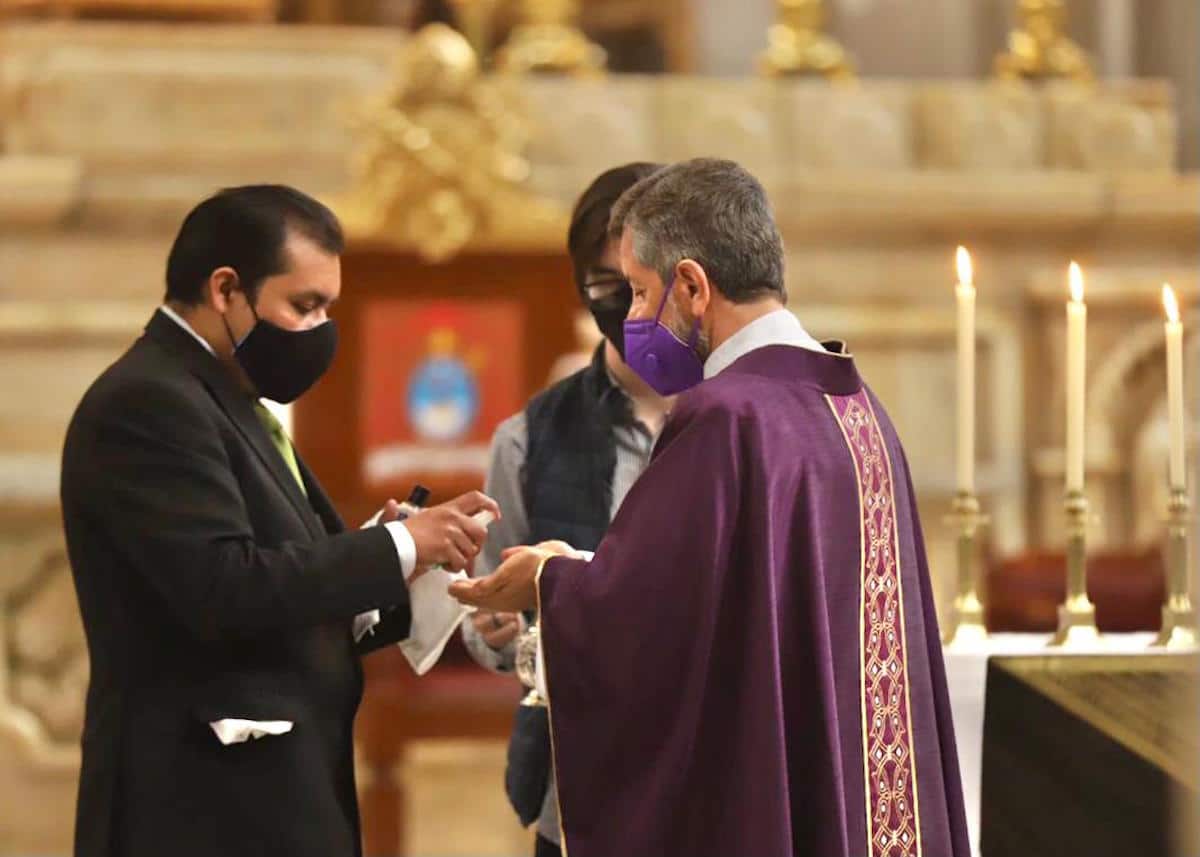 El padre Ricardo Valenzuela, deán de la Catedral de México, sanitiza sus manos con gel antes de imponer la ceniza a los fieles. Foto: María Langarica